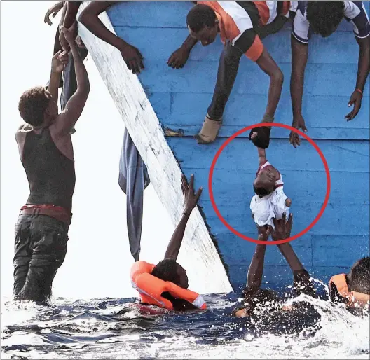  ??  ?? Life or death: Migrants desperatel­y try to hoist a baby (circled) out of the sea as they wait to be rescued off the coast of Libya