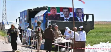  ??  ?? Russian forces allied with the Syrian regime distribute food next to Chechen, Syrian and Russian leaders’ portraits at the Abu al-Duhur crossing, to displaced Syrian families returning from rebel-held areas in Syria’s northern Idlib province to their...