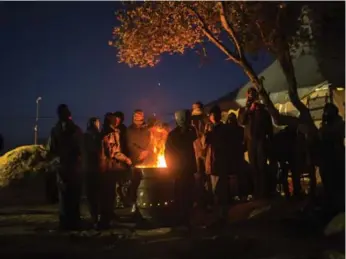  ?? SANTI PALACIOS/THE ASSOCIATED PRESS ?? Migrants try to keep warm next to a makeshift fire outside a registrati­on centre on the Greek island of Lesbos on Friday. More than a million people reached Europe in 2015, with more than 850,000 arriving on Greek shores.