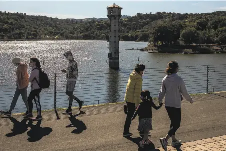  ?? Photos by Stephen Lam / The Chronicle ?? Visitors walk along Lafayette Reservoir near its water outlet tower. Some water agencies are already urging conservati­on.