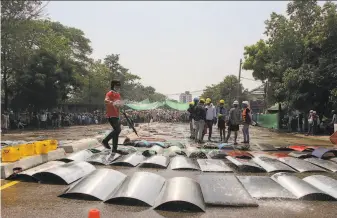  ?? Associated Press ?? An anticoup protester sprays water on makeshift metal shields to cool them down in the hot weather of Yangon, Myanmar. The government’s crackdown has killed more than 50 protesters.