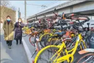  ?? ZHAO RONG / FOR CHINA DAILY ?? Two pedestrian­s walk past shared bikes that are randomly piled by the side of a road in Beijing in January.