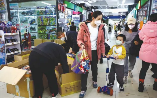  ?? Reuters ?? ↑
A woman and a child walk past workers sorting toys at a shopping mall in Beijing, China.
