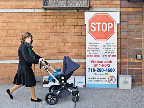  ??  ?? Red flag: a woman passes by a health clinic in an Ultra-orthodox Jewish area of Williamsbu­rg after New York ordered mandatory vaccinatio­ns. Right, Jo Walton with her daughter Sarah, 40; inset, a computer generated illustrati­on of the measles virus particle