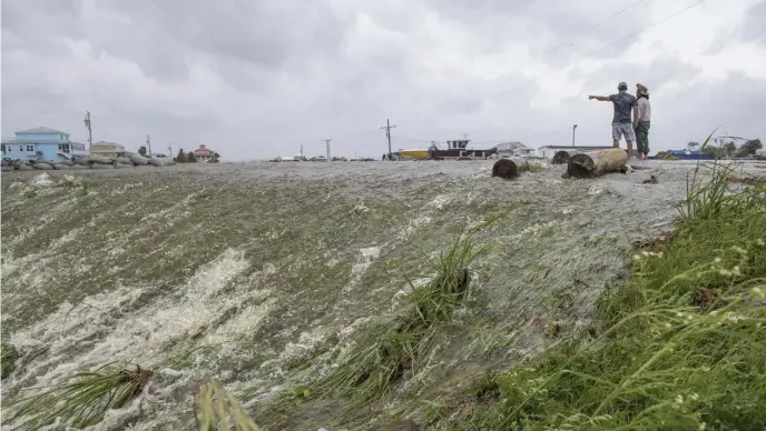  ?? AP ?? COASTAL THREATS: Chris Nguyen and his father, Trung, look at the moving water that breached the top of a levee just south of New Orleans as Hurricane Barry makes landfall Saturday.