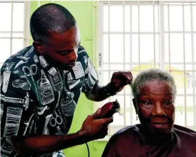  ??  ?? Eighty-year-old Mojeska Jarrett (right) from Garveymead­e is given a haircut by barber Romaine Johnson.