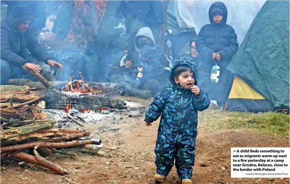  ?? Leonid Shcheglov/Associated Press ?? A child finds something to eat as migrants warm up next to a fire yesterday at a camp near Grodno, Belarus, close to the border with Poland