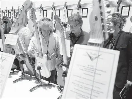  ?? John Gastaldo ?? BUYERS and music merchants look over custom-made Fender guitars on display at the NAMM Show in the Anaheim Convention Center. The trade show this year features more than 7,000 brands, made by a record 2,000 exhibiting companies, from more than 120...