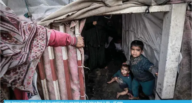  ?? ?? RAFAH: Displaced Palestinia­n children wait inside their makeshift tents at a camp beside a street in Rafah on March 14, 2024. — AFP photos