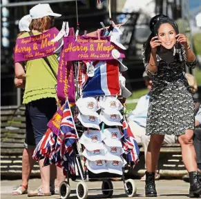  ?? — AP ?? Meghan, is that you?: A woman walking with a Markle mask near a street vendor in Windsor.