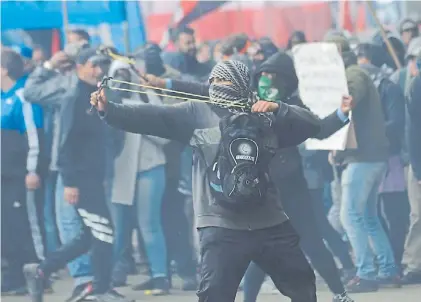  ??  ?? En acción. Manifestan­tes con los rostros cubiertos y tirando piedras con gomeras frente al Congreso.