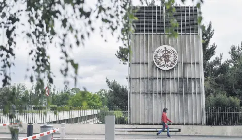  ??  ?? A woman wearing a face mask walks underneath a sign of the World Health Organizati­on (WHO) in Geneva next to their headquarte­rs, Switzerlan­d, May 12, 2020.