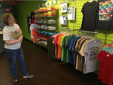  ?? RICHARD PAYERCHIN — THE MORNING JOURNAL ?? Cathy Kingsley, owner of Big Frog Custom T-Shirts & More in Avon, shows the colors available at the shop on April 15, 2020. Big Frog and the Lorain County Chamber of Commerce have launched a new “Lorain County Strong” T-shirt sale that raises money for a relief fund for small businesses struggling with closures and stay-at-home orders during the novel coronaviru­s pandemic.