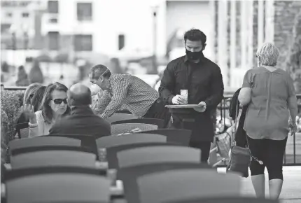  ?? DANIELLE PARHIZKARA­N/USA TODAY NETWORK ?? Diners sit outside at Haven Riverfront Restaurant and Bar on the first day New Jersey allowed restaurant­s to open for outdoor dining on June 15. A waiter wears a face mask while serving customers.