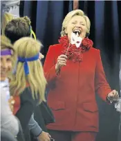  ?? Picture: REUTERS ?? UNMASKED: Hillary Clinton holds a Halloween mask while joking with her staff on her campaign plane