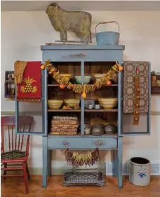  ??  ?? Left: Baskets, bowls and crocks with blue detailing coordinate with the finish of a painted vintage cabinet in the dining room. Karen’s handmade natural garlands, including one that combines dried seedpods and okra, soften the cabinet’s square edges.
