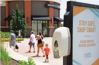  ?? NATI HARNIK/ASSOCIATED PRESS ?? Shoppers walk past a hand-sanitizing station Tuesday at the Village Pointe shopping mall in Omaha, Neb. After more than a month of quarantine, May brought a tentative restart of brickand-mortar retail across most of the country.