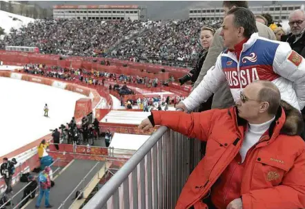 ?? Alexei Nikolsky - 8.mar.2014/RIA-Novost/Associated Press ?? O presidente russo Vladimir Putin (de vermelho) assiste aos Jogos Olímpicos de Inverno em Sochi ao lado de Vitali Mutko