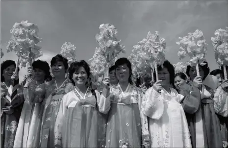  ??  ?? Women wearing traditiona­l Korean dress hold plastic flowers as they stand at a roadside during an “internatio­nal march for peace, prosperity, and reunificat­ion of Korea” at the Three Charters Monument on the outskirts of Pyongyang on Tuesday.