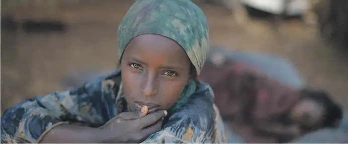  ??  ?? A young girl sits in the shade, while her sister sleeps behind her, at an IDP camp in Baidoa for victims of a drought currently affecting Somalia