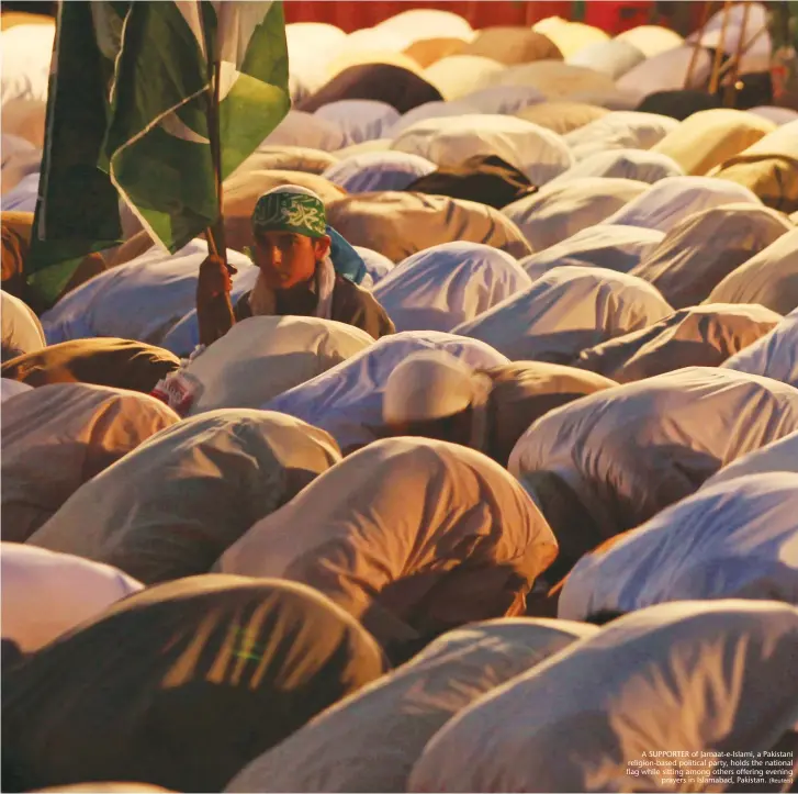  ??  ?? A SUPPORTER of Jamaat-e-Islami, a Pakistani religion-based political party, holds the national flag while sitting among others offering evening prayers in Islamabad, Pakistan.