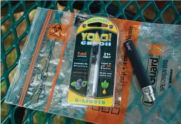  ?? Associated Press ?? ■ A Yolo! brand CBD oil vape cartridge sits alongside a vape pen on a biohazard bag on a table at a park in Ninety Six, S.C. More than 50 people around Salt Lake City had been poisoned by the time the outbreak ended early last year, most by a vape called Yolo!, the acronym for “you only live once.”