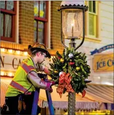  ?? BY HUGO MARTIN ?? A WORKER fastens a wreath to a lamppost on Main Street U.S.A. in preparatio­n for the Anaheim resort’s holiday season.