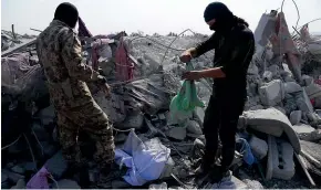  ?? AP ?? Unidentifi­ed masked men examine destroyed houses near the village of Barisha after an operation by the US military which targeted Abu Bakr alBaghdadi.