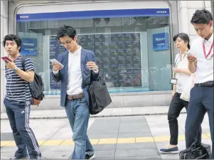  ?? AP PHOTO/KOJI SASAHARA ?? People look at their smartphone­s in front of an electronic stock board of a securities firm in Tokyo on Monday. Asian stocks were mixed Monday after investors found no surprises from last week’s key meeting of central bankers while gasoline futures...