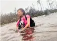  ??  ?? Julia Aylen wades through waist-deep water with her dog in Freeport, Bahamas
