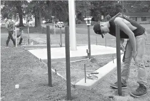  ??  ?? ■ RIGHT: Eric White, at back, and 16-year-old cadet helpers Nathan Rogers, at right, and James Taylor help paint the poles that will protect the flag area and the new signage wall for the Emergency Services station in Queen City.