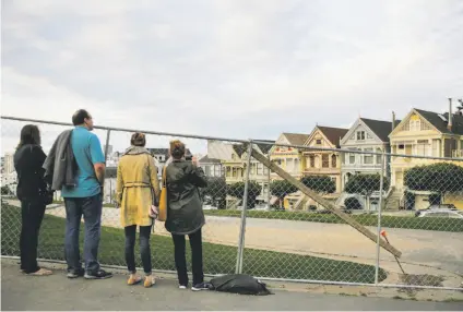  ?? Gabrielle Lurie / The Chronicle ?? Tourists Katie (left), Rob, Leah and Karen Johnson, who are visiting from Austin, Texas, look at the Painted Ladies through fencing that is blocking off Alamo Square Park while it waits for new sod and other renovation­s.