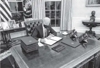  ?? DOUG MILLS The New York Times ?? President Joe Biden signs executive orders during his first minutes in the Oval Office of the White House in Washington on Wednesday.