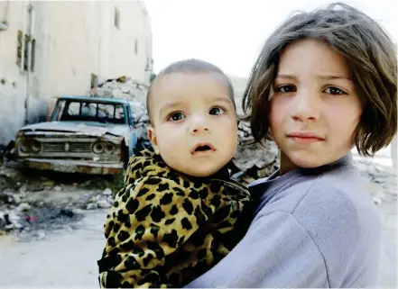 ??  ?? طفلة سورية تحمل أخاها، تقف في شارع مدمر في مدينة دوما أمس األول. (أ.ف.ب)