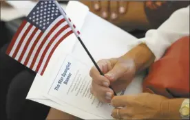  ?? AP photo ?? A citizen candidate holds an American flag and the words to “The Star-Spangled Banner” before the start of a naturaliza­tion ceremony at the U.S. Citizenshi­p and Immigratio­n Services field office in Miami on Friday.