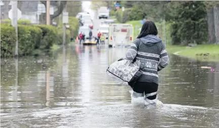  ?? ALLEN MCINNIS ?? May 7: With her legs wrapped in plastic, Annick Sauvé leaves her flooded home in Laval and makes her way toward waiting firefighte­rs.