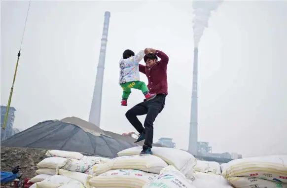  ??  ?? Yang Zhongliang svinger sønnen sin i en seiersdans på toppen av varene de har fraktet til Chongqing. De feirer at deres største last dette året,10 000 sekker med korn, er kommet vel frem. Familien Yang eier lastebåten som de bruker til å frakte varer på Yangtze-elven, mellom Chongqing og Shanghai. Familien på åtte personer – bestefar, bestemor, to sønner, en datter og hennes mann, og to barnebarn – bor om bord i båten og møter sjelden andre mennesker enn bryggesjau­erne som laster og losser varene de frakter.