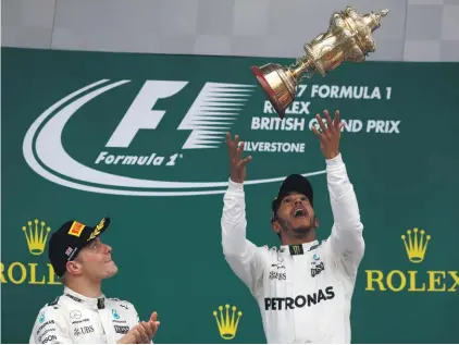  ??  ?? Second placed Mercedes driver Valtteri Bottas, left, applauds as teammate Lewis Hamilton celebrates on the podium after winning at Silverston­e Photo: AP