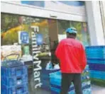  ?? ?? Deliveryma­n Jiang Cheng waits in front of the FamilyMart store on Xincun Road. The door is open just wide enough for staff to hand out plastic bags. — Zhou Anna