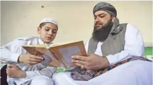  ??  ?? This picture shows Maulana Mohammad Tayyab Qureshi (right), the imam of the main Peshawar mosque, teaching with an Islamic book to his son at the mosque in Peshawar.