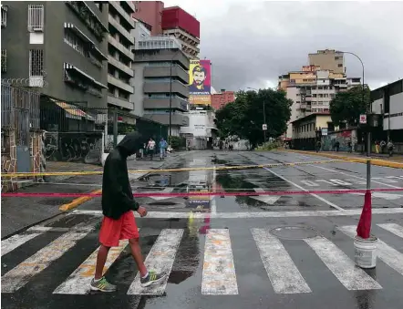  ??  ?? Homem caminha por rua de Caracas em dia de proibição de protestos pelo governo e bloqueios de vias pela oposição