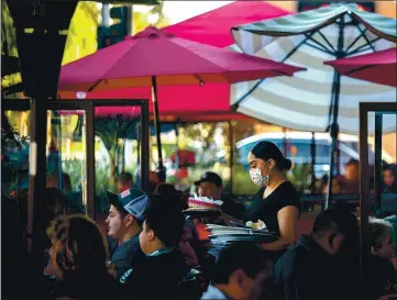  ?? PHOTO BY WATCHARA PHOMICINDA — MEDIANEWS GROUP/ THE PRESS-ENTERPRISE ?? A server clears a table as patrons dine outdoors at a restaurant in Ontario, California. In July, Gov. Gavin Newsom said that he would target businesses that flagrantly violate public health orders. As coronaviru­s cases surge across California, however, businesses have faced few, if any, consequenc­es.