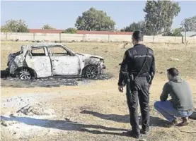  ??  ?? Un policía mira un coche calcinado cerca del lugar de los hechos.