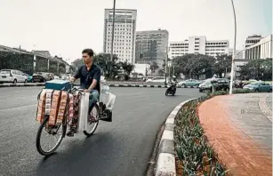  ??  ?? Caffeine for cash: An instant coffee seller cycling past a main road in Senen, Central Jakarta. — The Jakarta Post/ ANN