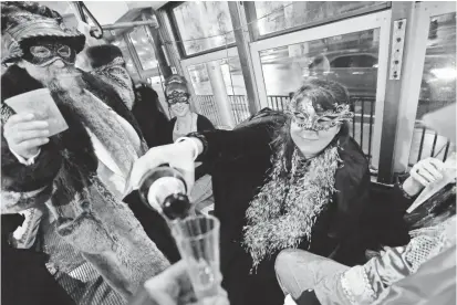  ?? GERALD HERBERT/AP ?? Members of the Societe des Champs Elysee riding the Rampart-St. Claude streetcar line pour Champagne to commemorat­e the official start of Mardi Gras season Friday in New Orleans.