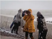  ?? POLLY THOMAS GETTY IMAGES ?? People walk through flying sea foam spray on Sunday in Porthcawl, Wales. Gusts from the storm reached 150 km/h.