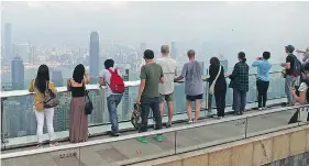  ??  ?? Tourists enjoy the view of Hong Kong skyscraper­s and harbour from Victoria Peak after a steep tram ride.