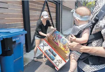  ?? ERIN HOOLEY/CHICAGO TRIBUNE PHOTOS ?? Kelly Pickering, with her husband, Dan White, and their 6-month-old daughter Coco, find a discarded He-Man toy box in an alleyway in their neighborho­od July 19 in Chicago.