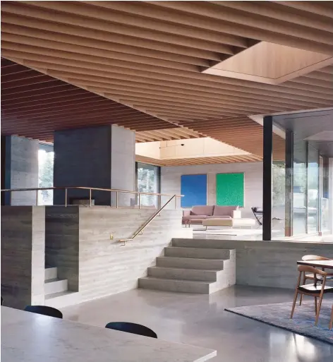  ??  ?? ABOVE: A concrete staircase paired with a polished brass handrail leads from the kitchen and dining area to the elevated living room above it. The house’s internal topography reflects the sloping landscape outside.