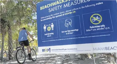  ?? EFE/ GIORGIO VIERA ?? Un hombre en bicicleta pasa delante de un cartel que pide respetar las medidas de seguridad, en Miami, ayer.